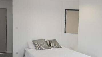 A minimalist bedroom with a single bed, a window, and a wooden floor.