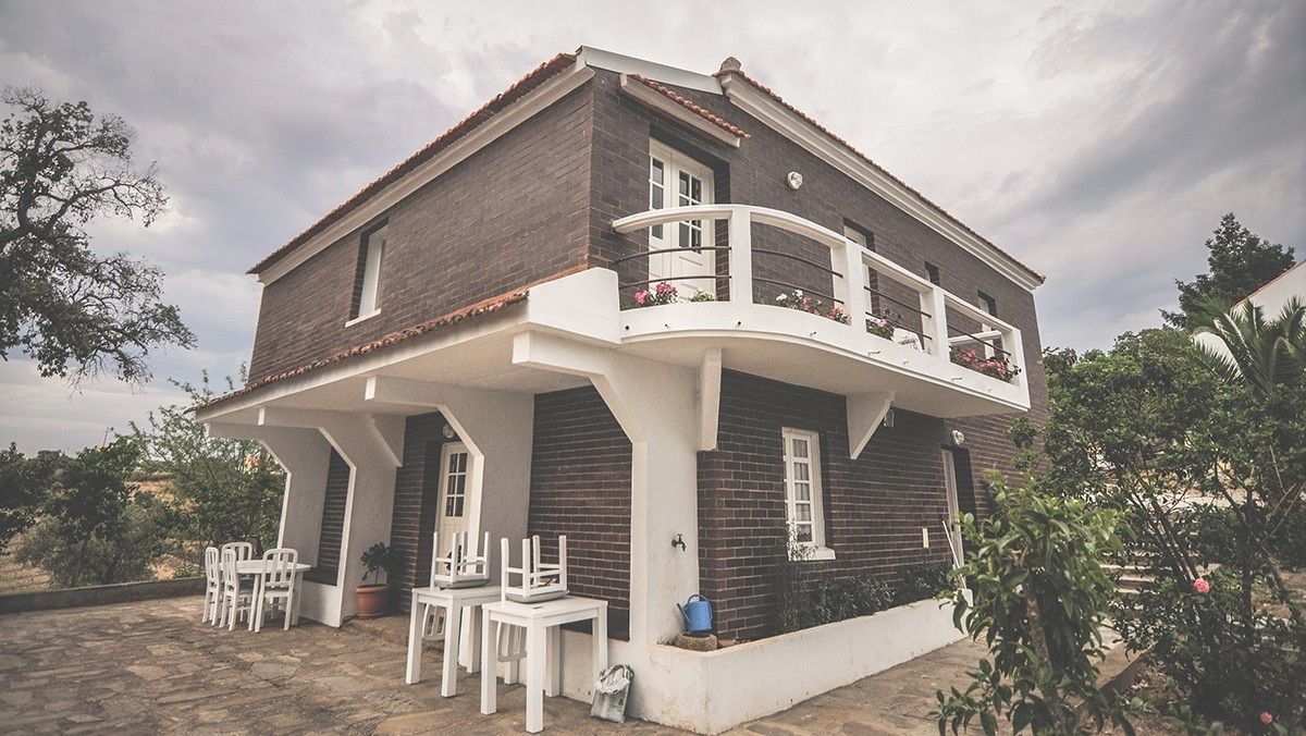 Une maison à deux étages avec un balcon, une terrasse dotée de meubles blancs et un jardin.