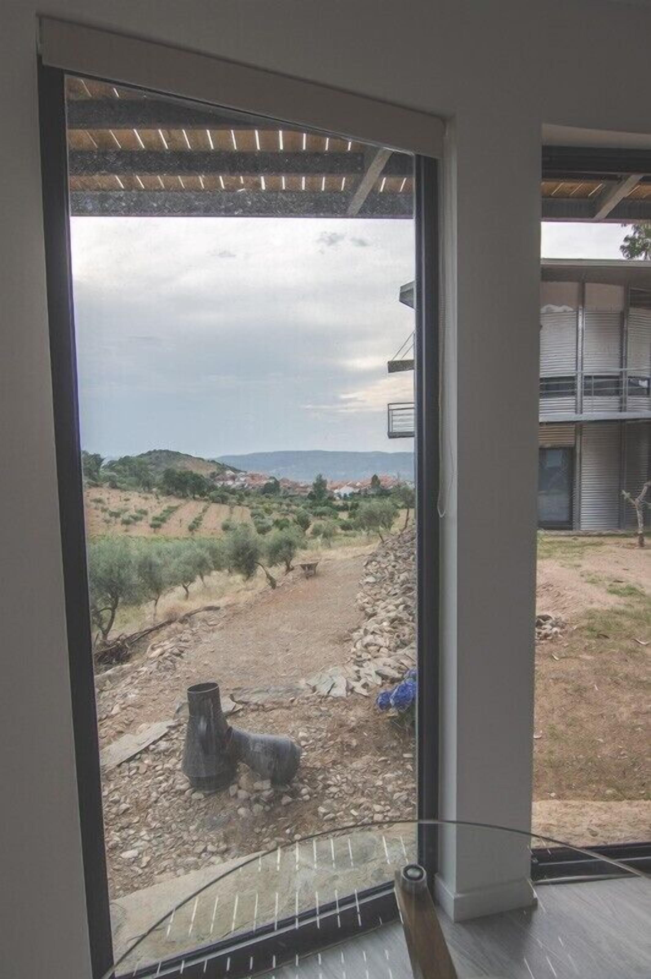 A view from a balcony with a metal railing, overlooking a dry landscape with sparse vegetation and a distant mountain range.