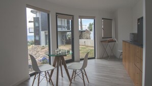 Eine moderne Küche mit einem Glastisch und Stühlen, großen Fenstern und Blick auf den Garten.