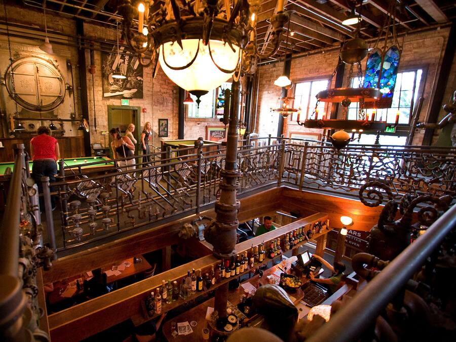 A bar with a pool table, a bartender, and a variety of bottles.