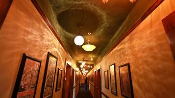 A hallway with framed pictures on the walls, a staircase at the end, and hanging lights.