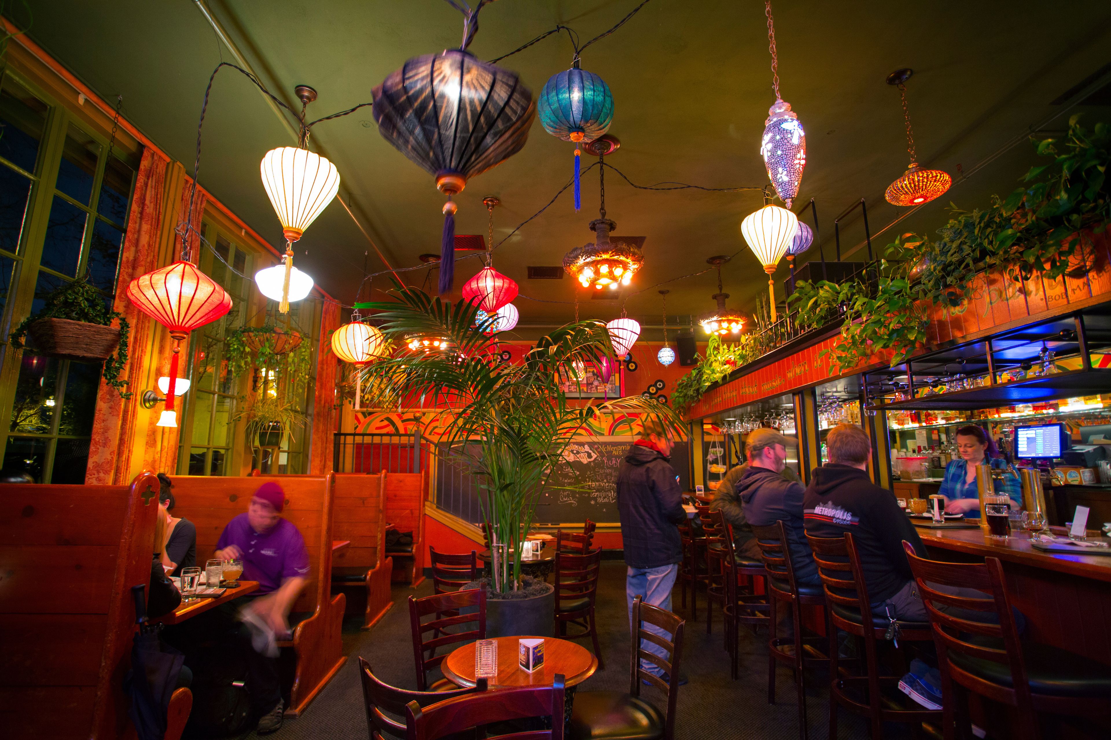 Un restaurant doté de nombreuses tables et chaises, de luminaires décoratifs suspendus et d’un espace bar.