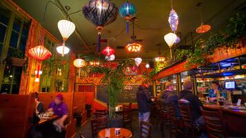 Un restaurant doté de nombreuses tables et chaises, de luminaires décoratifs suspendus et d’un espace bar.