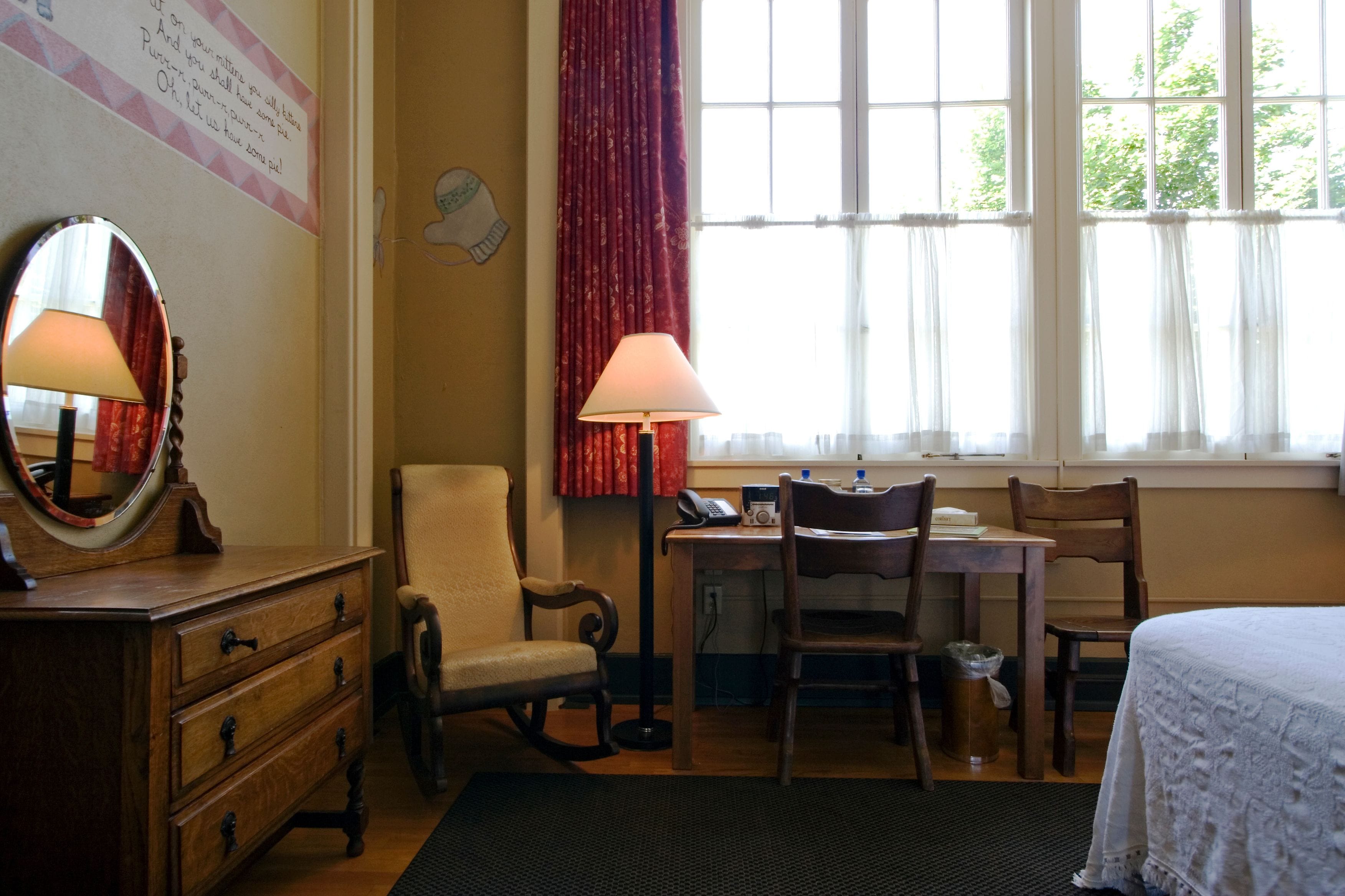 Et værelse med et træmøbel, en stol, et skrivebord med lampe og en seng.