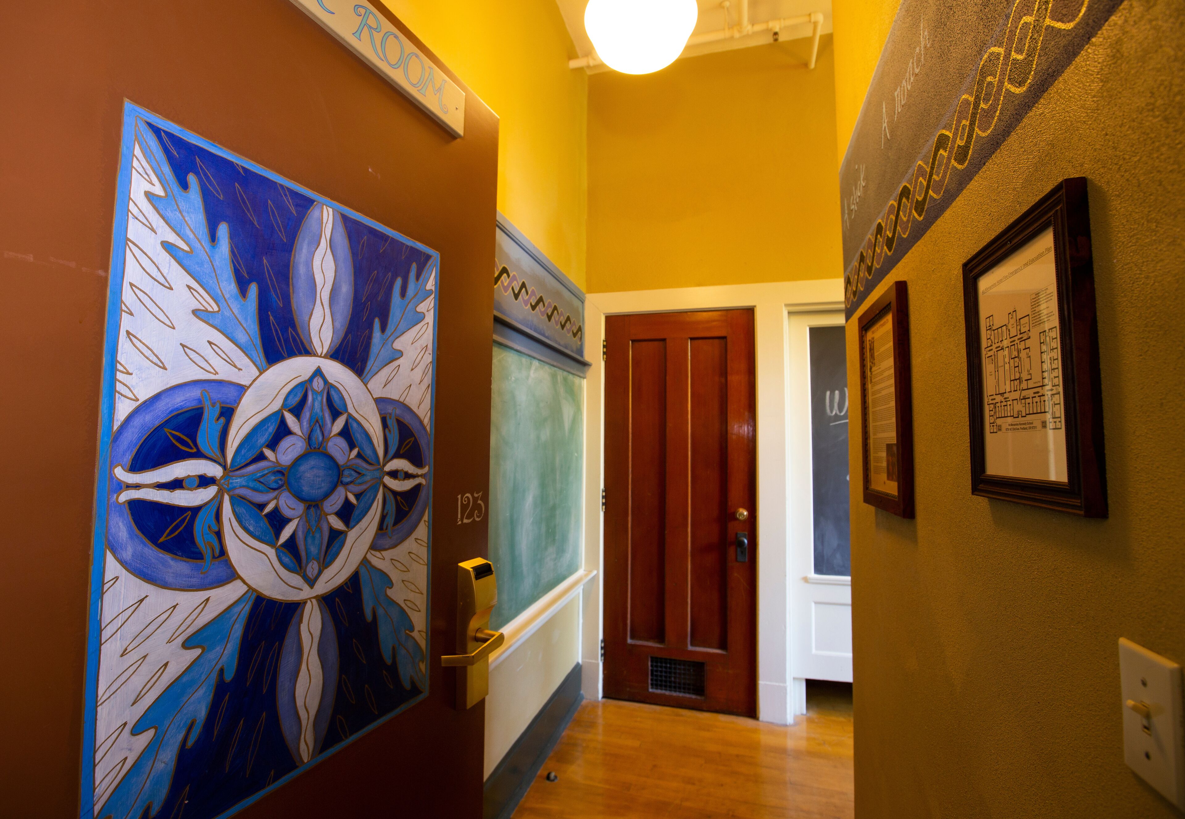 Um corredor com um grande mural floral, uma porta com a inscrição "123" e obras de arte emolduradas nas paredes.
