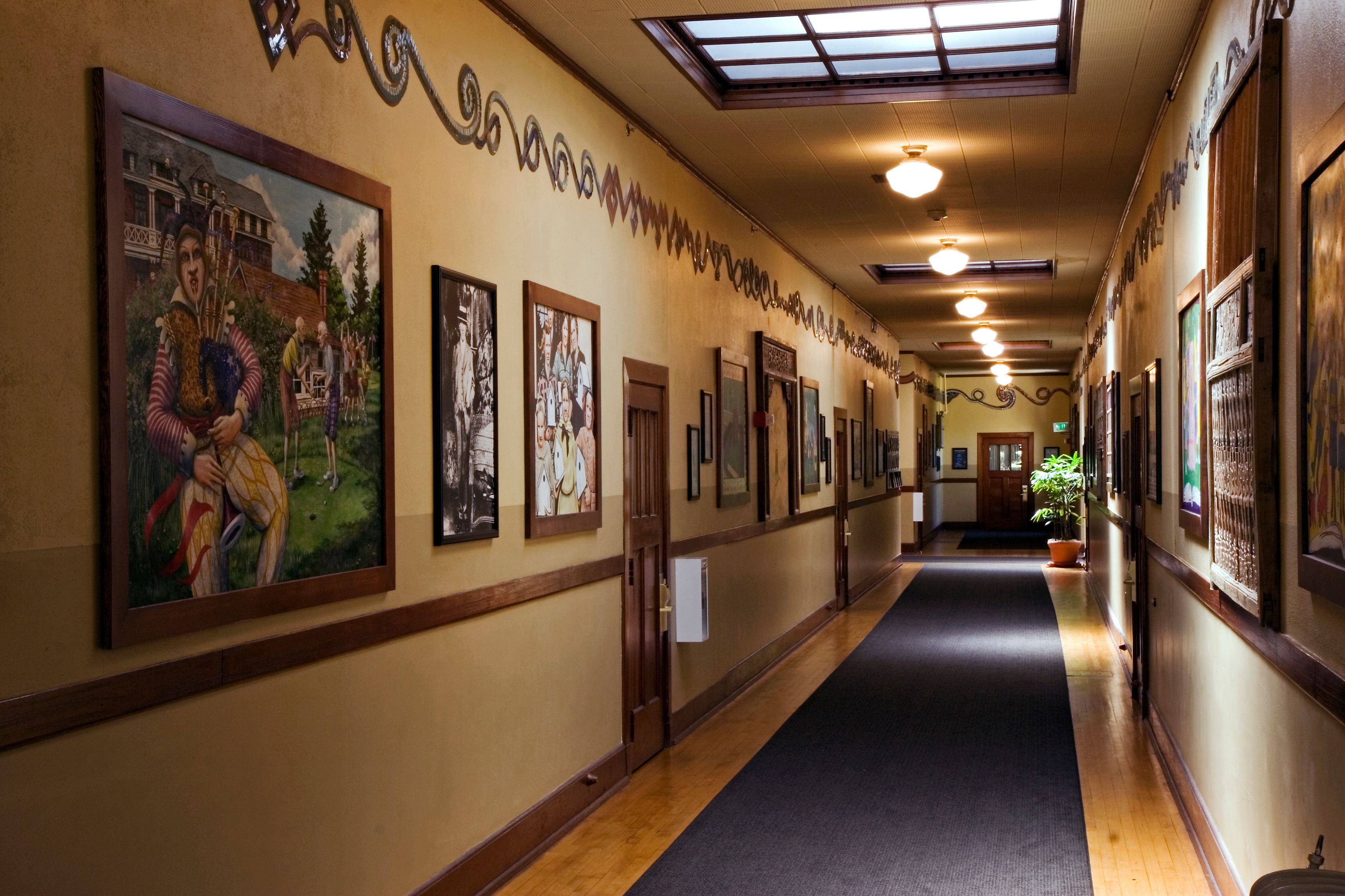 A long hallway with framed pictures on the walls, wooden doors, and a skylight.