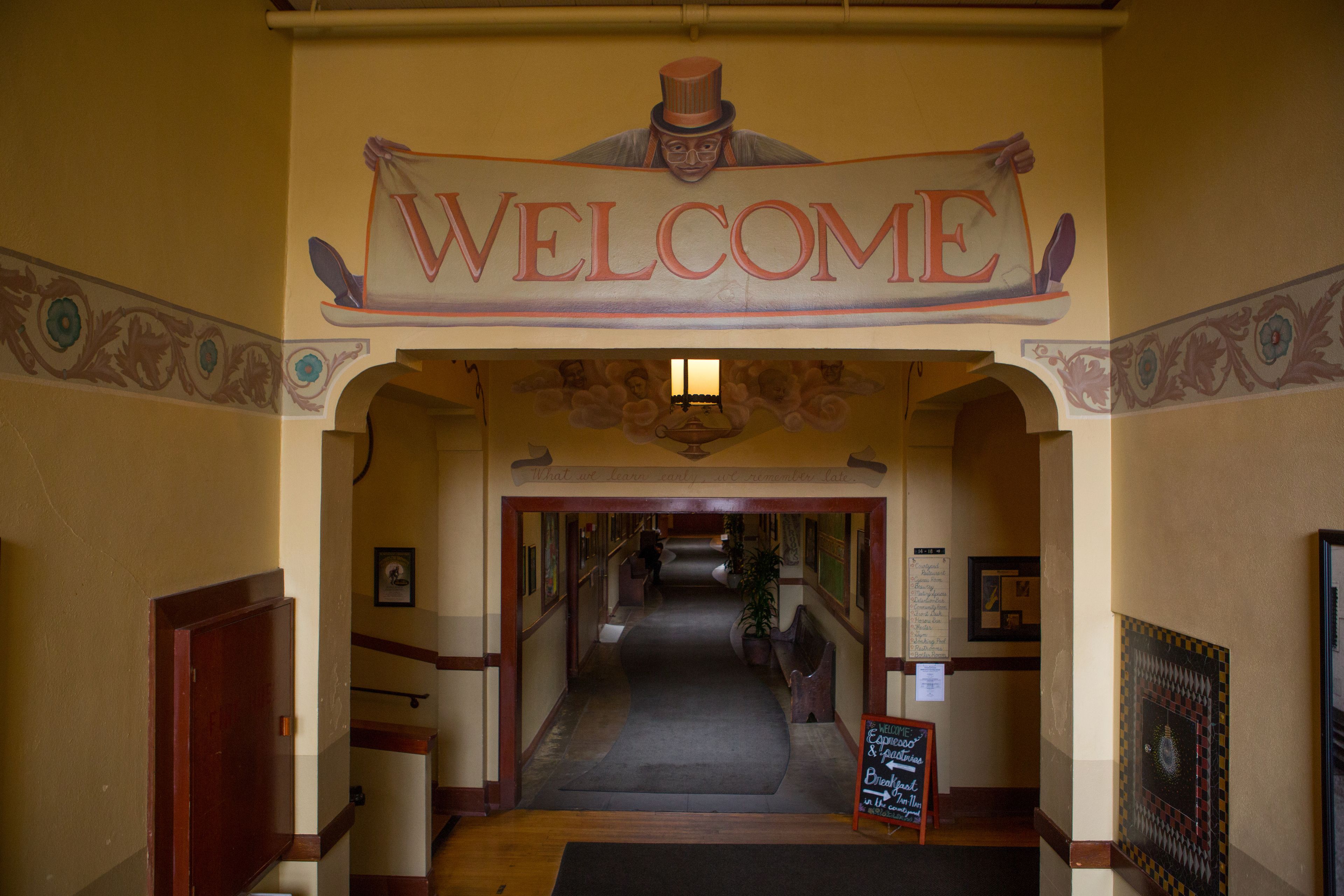 A hallway with a 'WELCOME' sign, framed by decorative arches and a carpeted floor.