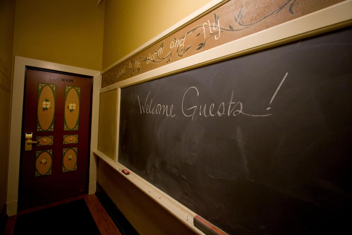 A blackboard with "Welcome Guests!" written on it, a door with decorative panels, and a wall with a decorative sign above the door.