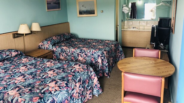 A hotel room with two single beds, a small table, a chair, a sink, and a mirror. - Friendly Inn Motel (Harrisburg)