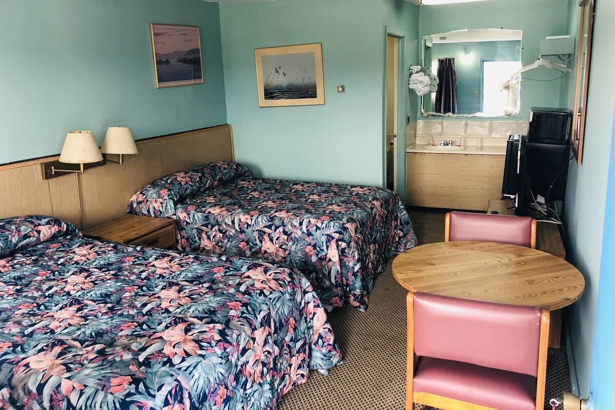 Habitación de hotel con dos camas individuales, una mesita, una silla, un lavamanos y un espejo.
