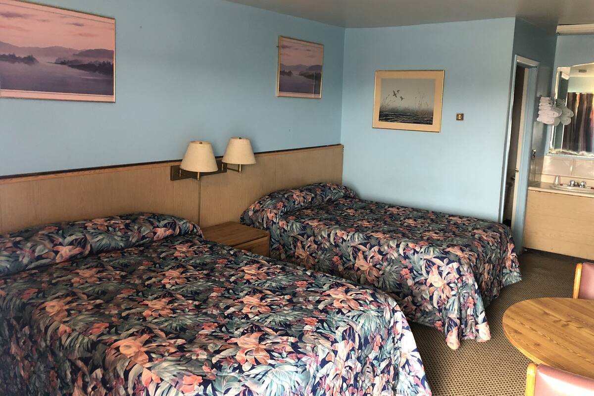 Una habitación con dos camas, un cabecero de madera, dos lámparas fijadas a la pared y una pequeña mesa redonda.