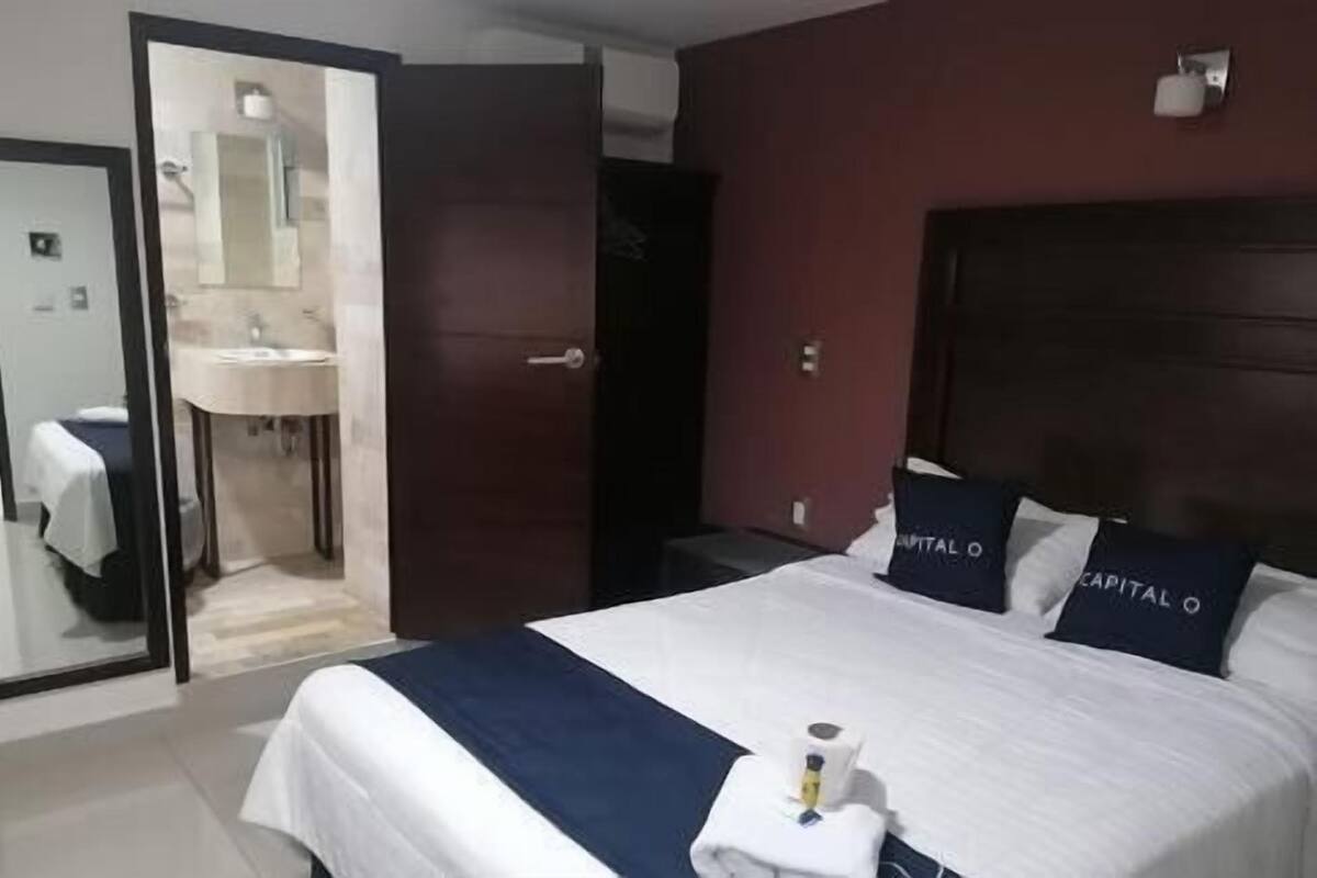 A hotel room with a bed, a mirror, a bathroom, and a door.