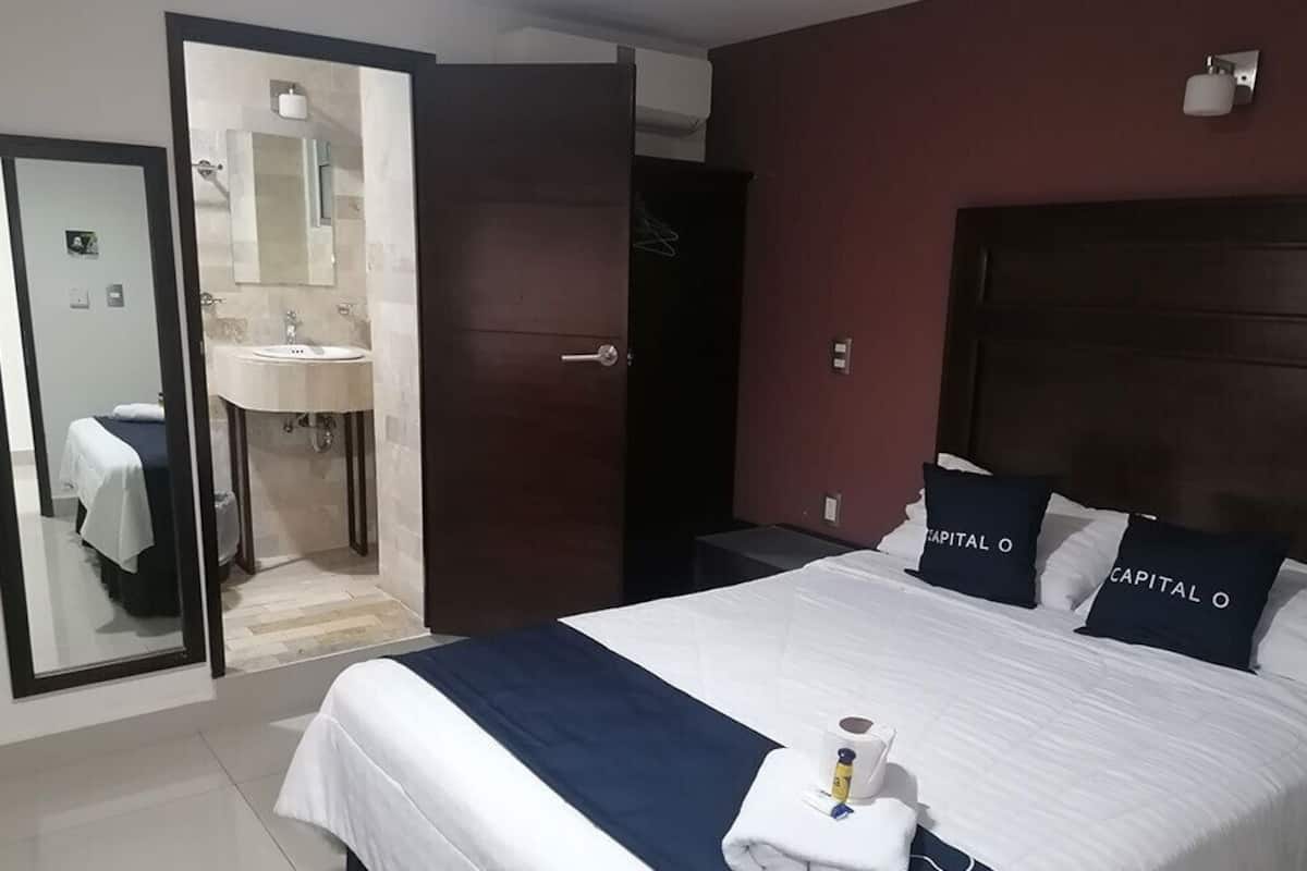 A hotel room with a bed, a bathroom with a sink, and a mirror.
