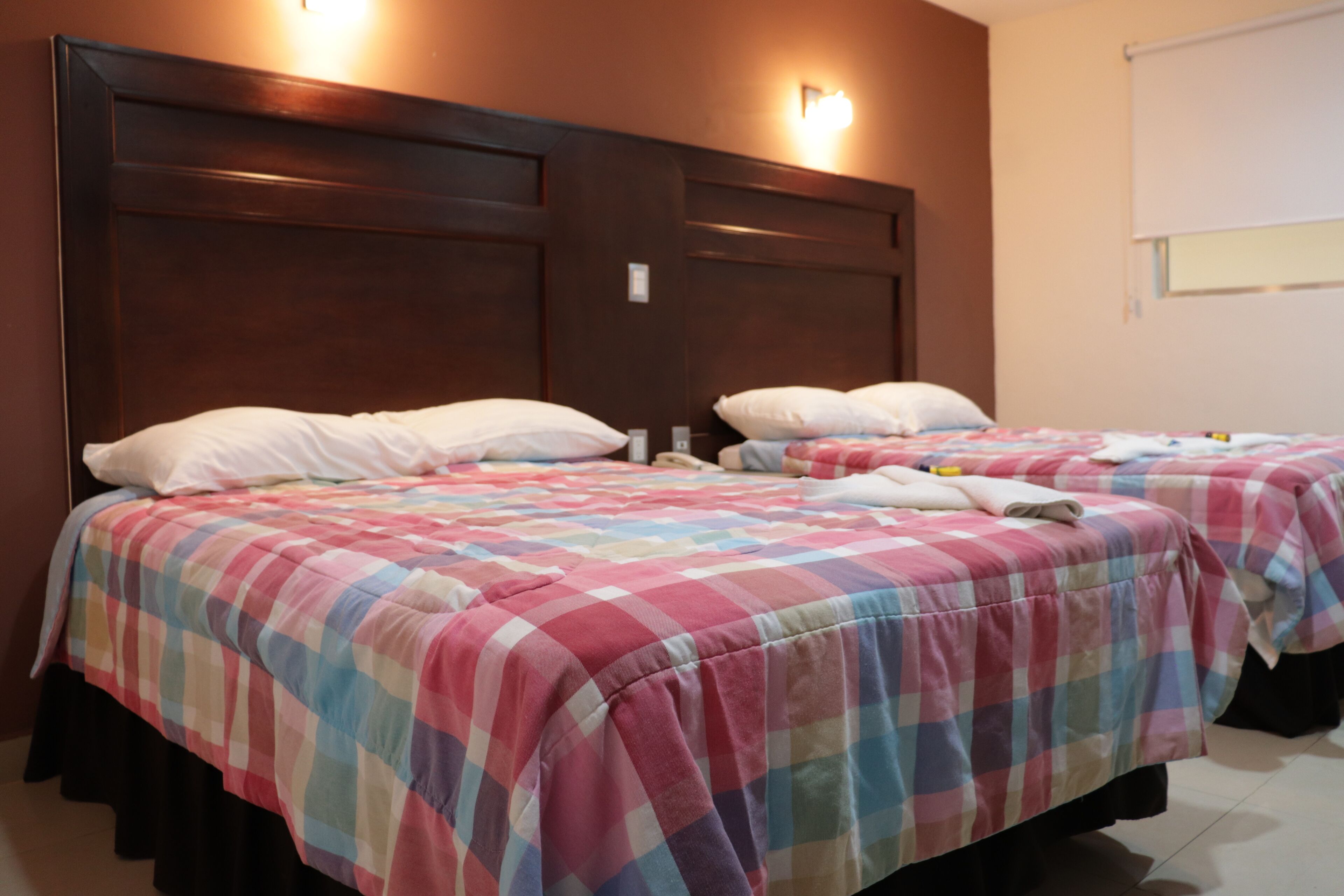 A hotel room with two beds, each with a colorful checkered bedspread and white pillows.