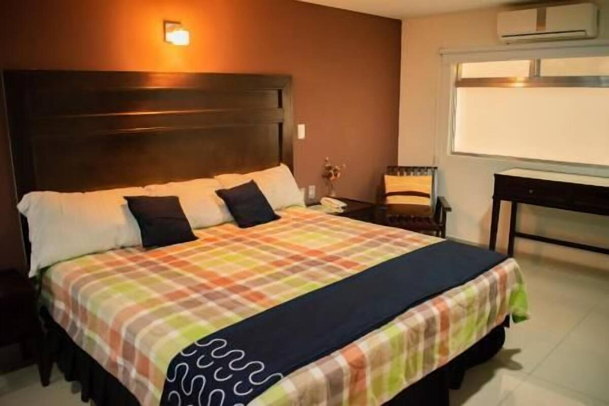 A hotel room with a bed, nightstands, a desk, and a window.