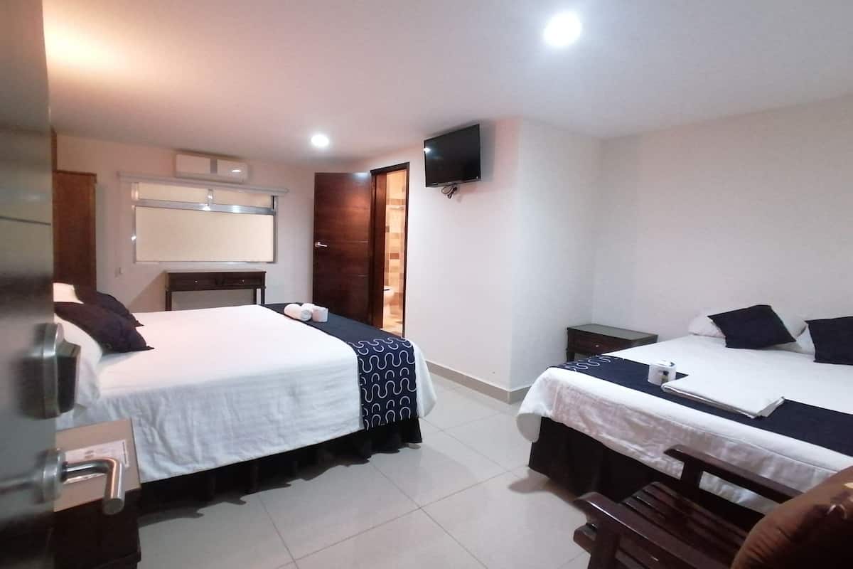 A hotel room with two beds, a TV mounted on the wall, a mirror, and a wooden bench.