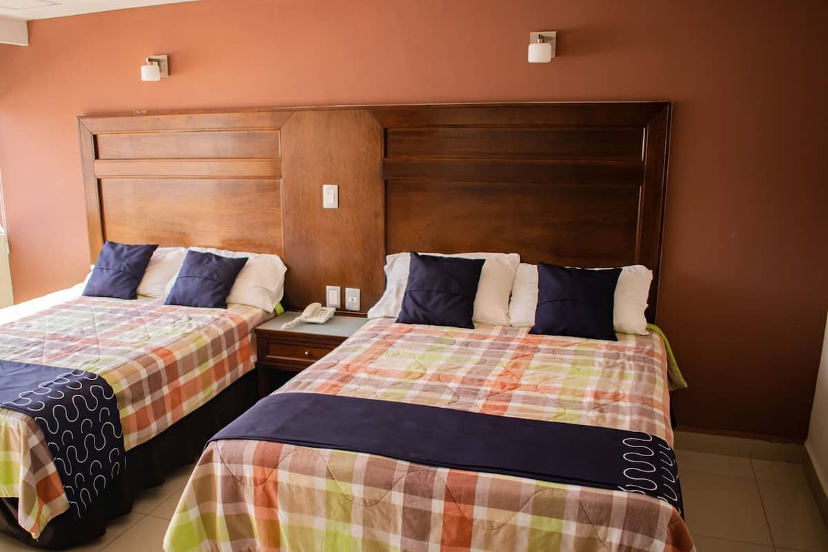A hotel room with two beds, each with a checkered bedspread, a wooden headboard, bedside lamps, and a telephone on the nightstand.