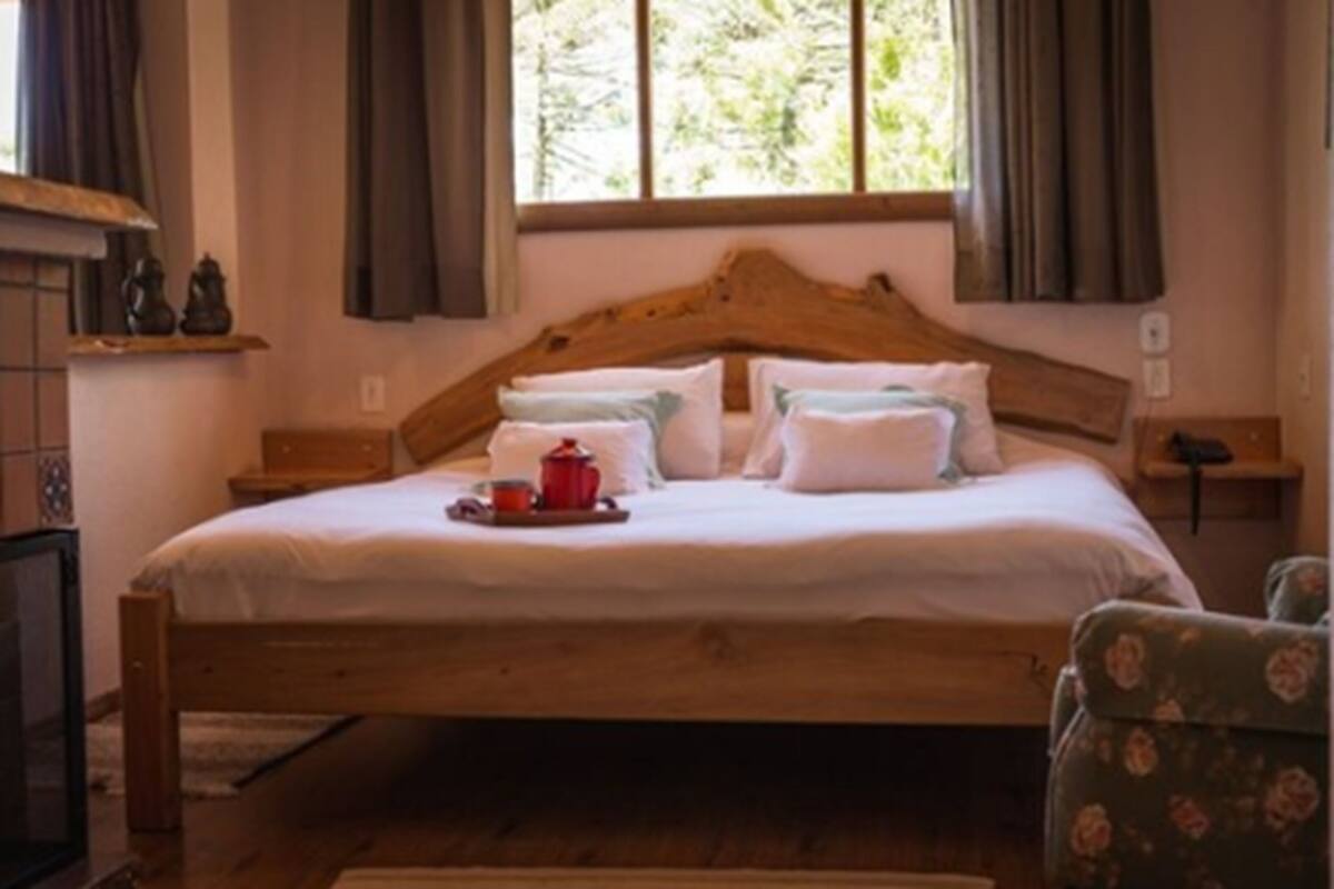 Una cama de madera con ropa de cama blanca, una bandeja con tetera y tazas, y una silla con tapicería floral.