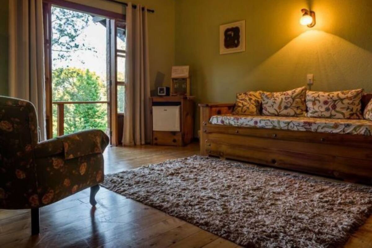 Una habitación acogedora con un sofá de madera, un sillón estampado, un escritorio pequeño y un ventanal con cortinas.