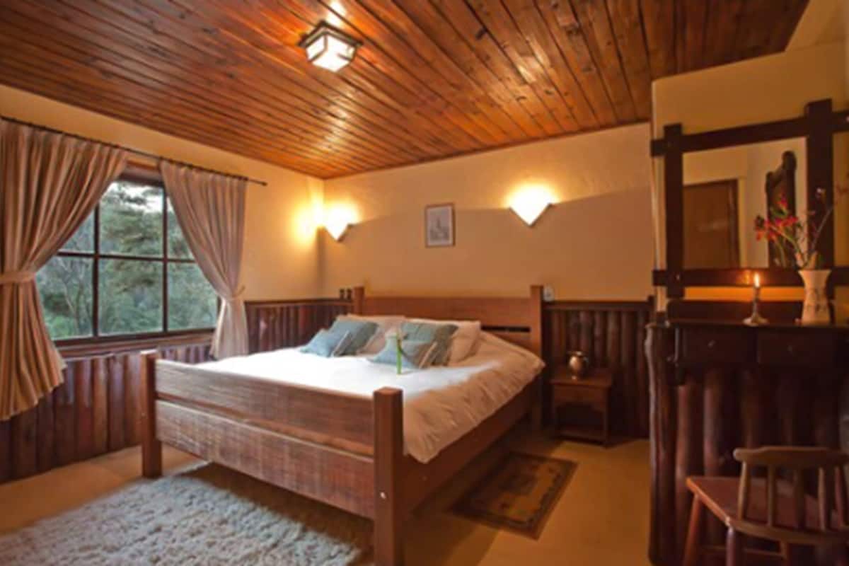 Un dormitorio con paneles de madera, una cama, dos apliques, un espejo y un ventanal con cortinas.