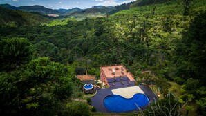 Une maison avec une piscine, entourée d’une végétation luxuriante et de collines.