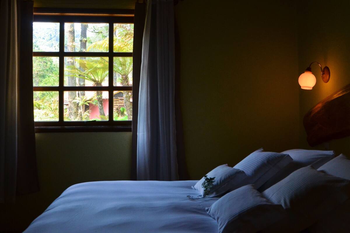 Un dormitorio con un ventanal grande, una cama con almohadas y una lámpara fijada a la pared.