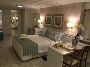 A hotel room with a bed, bedside table, lamp, framed artwork, and a desk with a chair. - Palace Hotel (Campos)