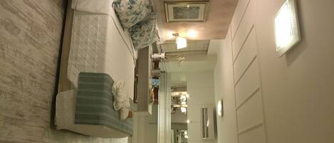 A modern hotel room with a bed, a seating area, a bathroom, and a hallway leading to the entrance.
