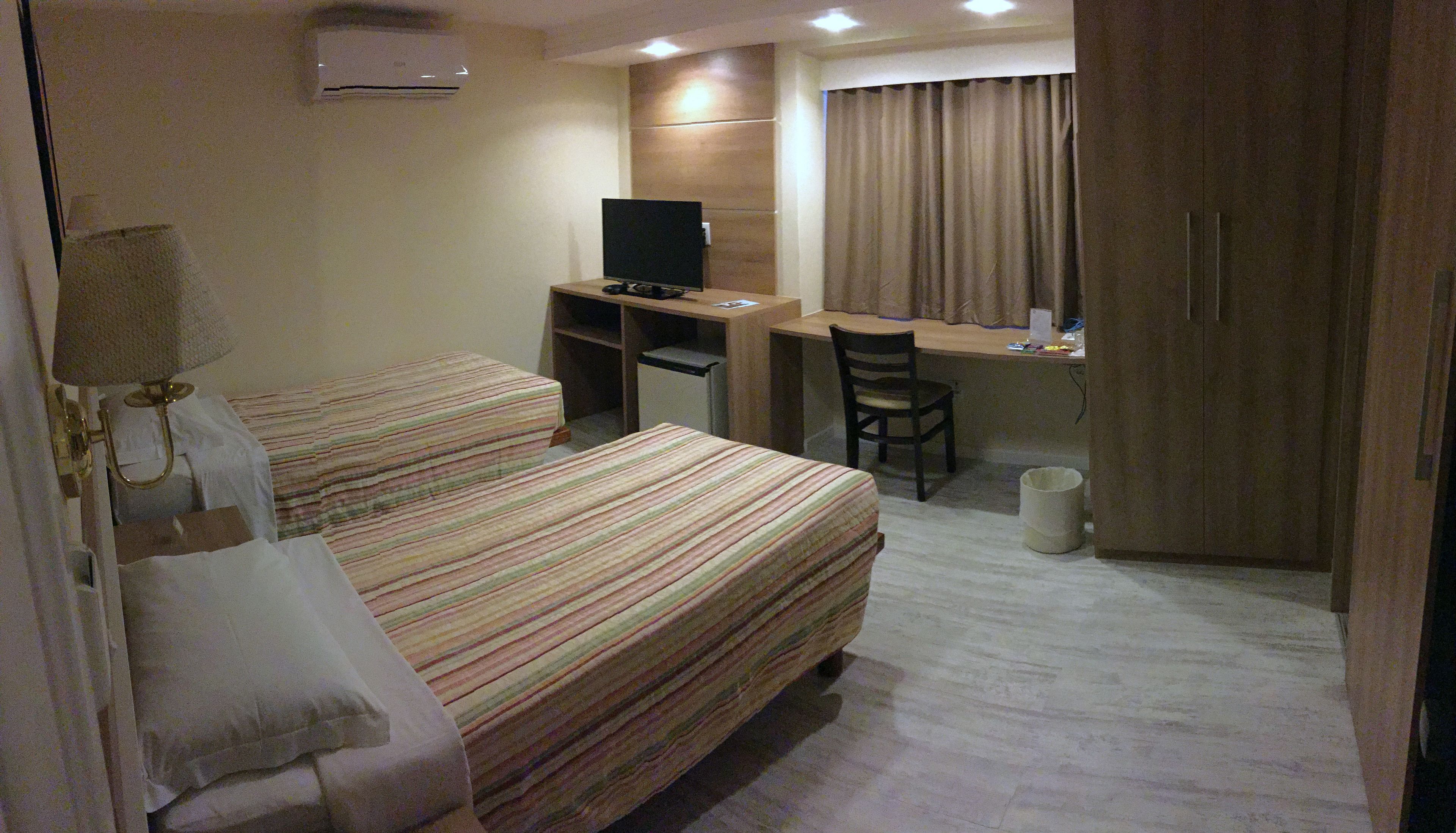 Habitación de hotel con dos camas, un escritorio, una silla, un televisor y un armario.