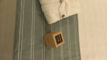 A bed with a striped pillow and two white robes on it.