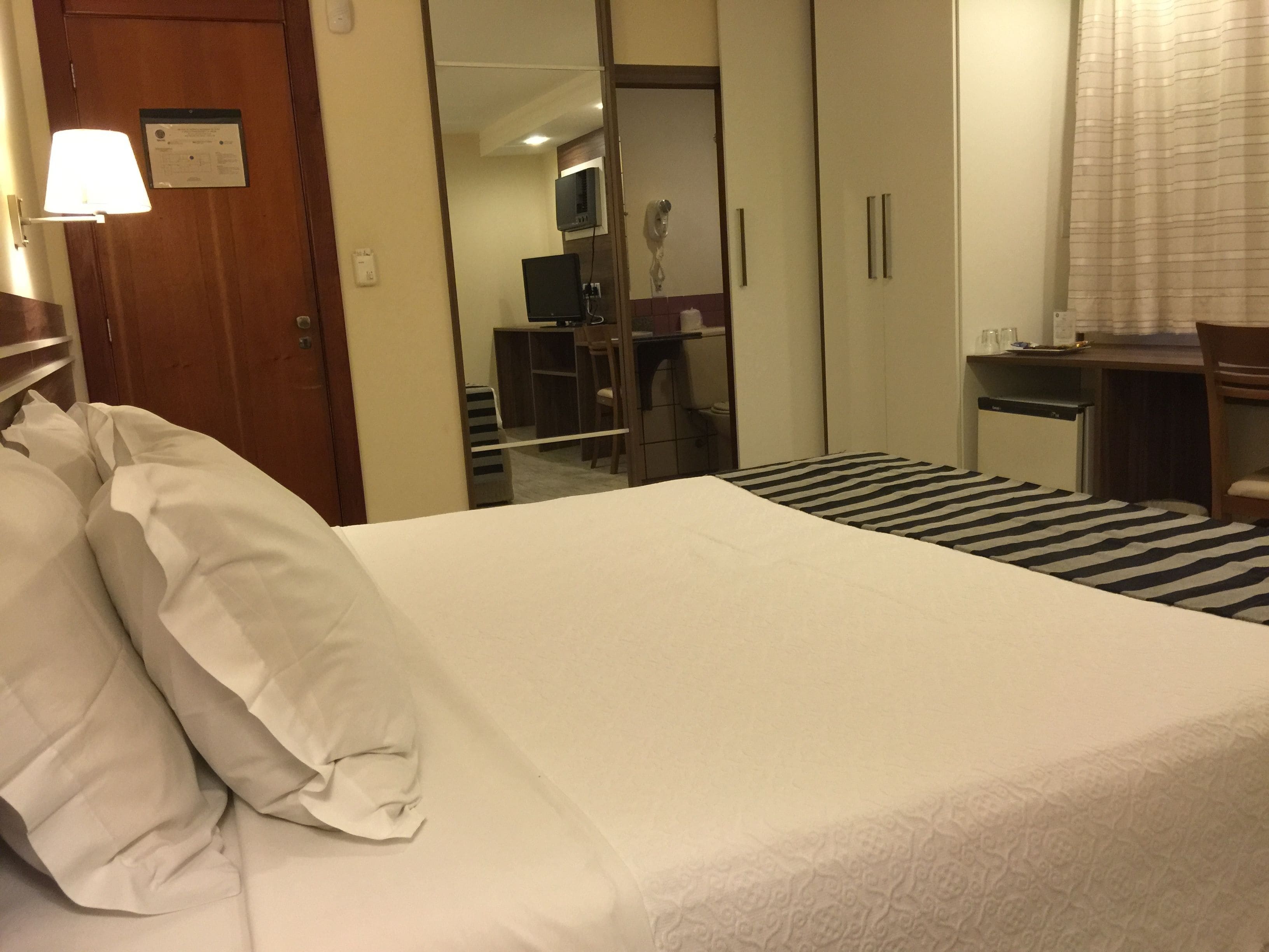 Een hotelkamer met een bed, bureau, stoel en spiegel.