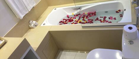 Ein Badezimmer mit einer Badewanne, gefüllt mit Rosenblättern, einer Toilette, einem Waschbecken und einer kleinen Topfpflanze.