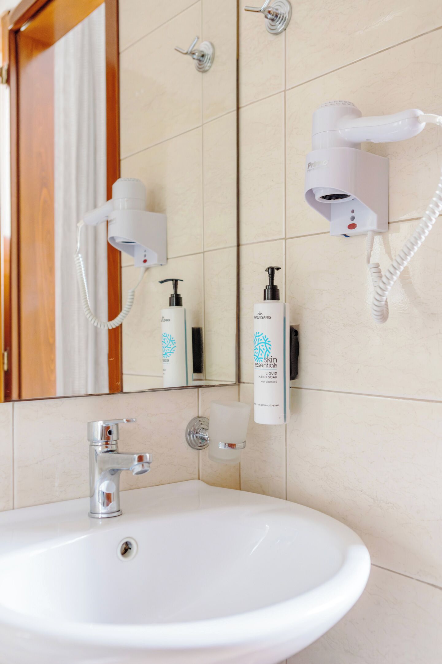 Un baño con lavamanos blanco, un espejo, un secador de pelo y una botella de jabón líquido para manos.