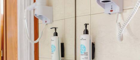 A bathroom with a white sink, a mirror, a hairdryer, and a bottle of liquid hand soap.