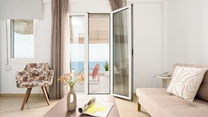 Una sala de estar moderna con un sofá, una silla, una mesa de centro con una revista, un jarrón con flores y vista al mar a través de una puerta corredera.