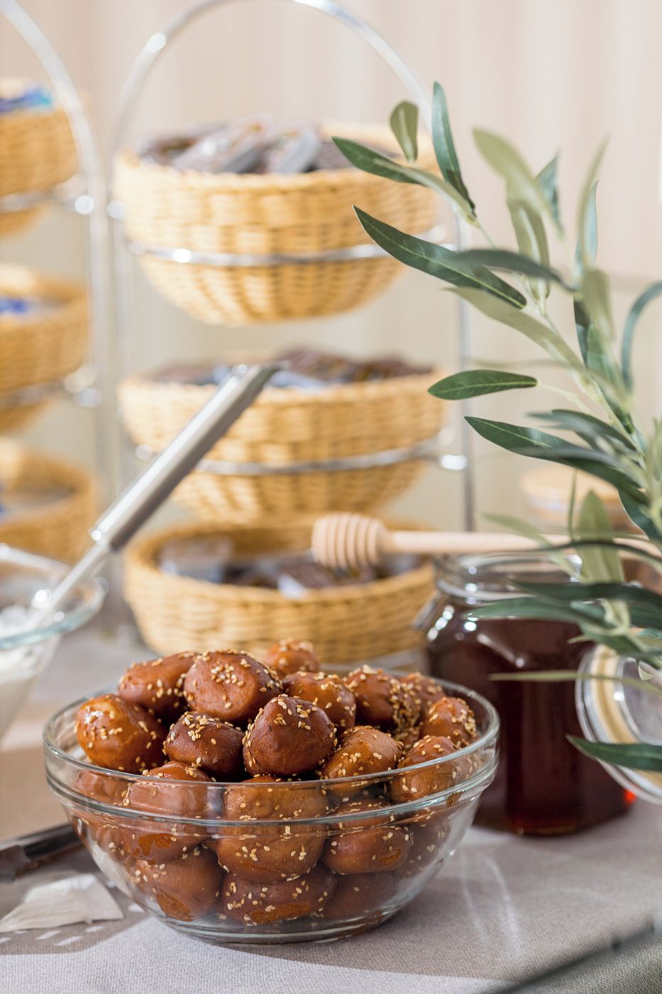 A glass bowl filled with sesame seed-covered sweets, a honey dipper, and a jar of honey.