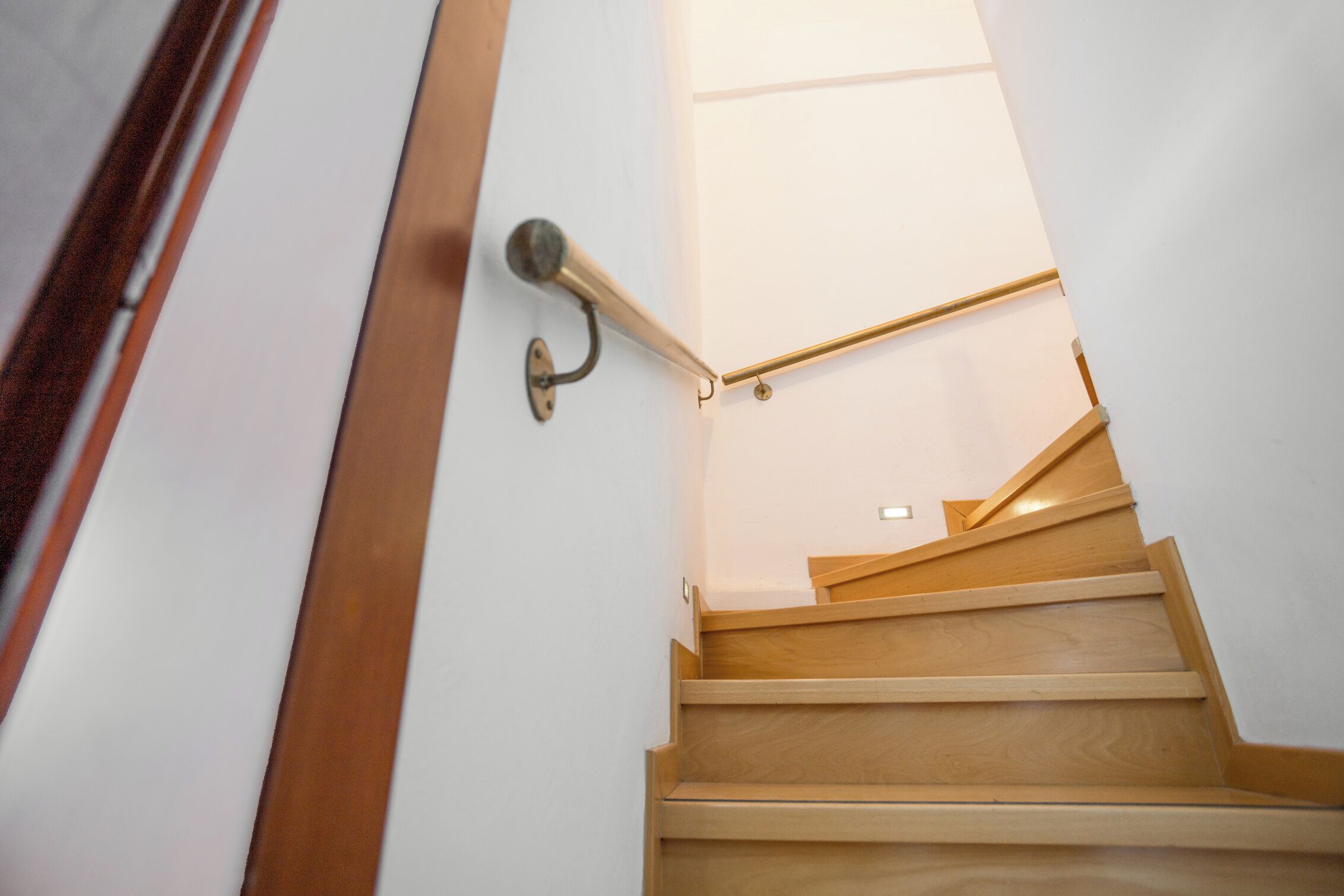 Una escalera de madera con barandilla metálica y una puerta con picaporte redondo.