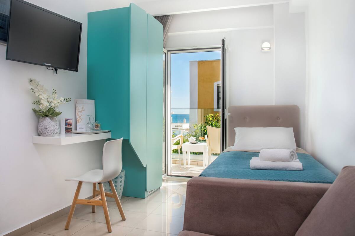 A modern hotel room with a bed, a desk, a chair, a TV, and a balcony with a view.