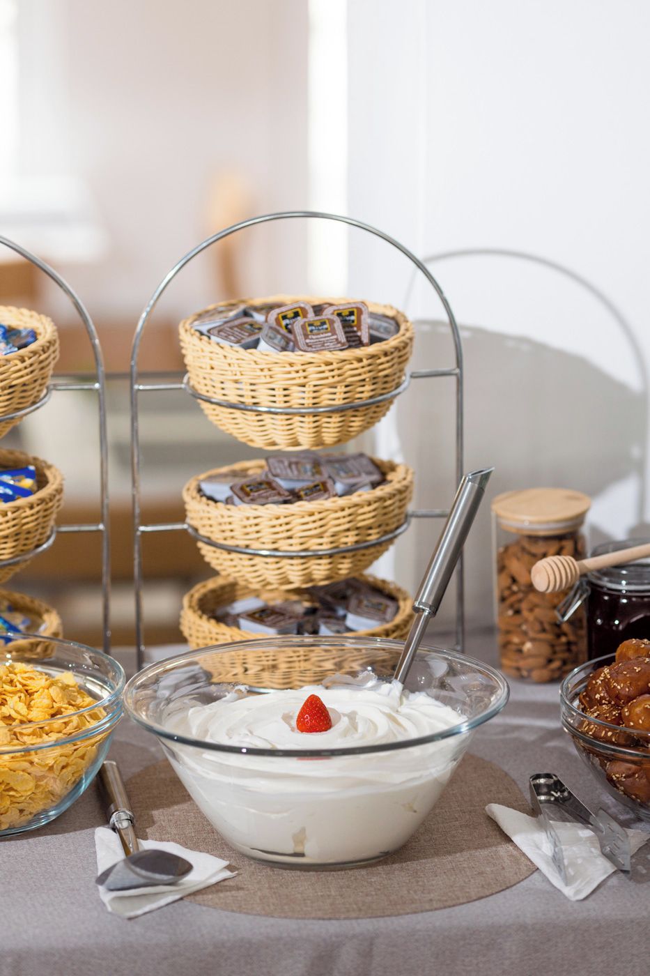 A buffet setup with a bowl of yogurt parfait, a tiered wicker basket with chocolates, and a jar of honey.