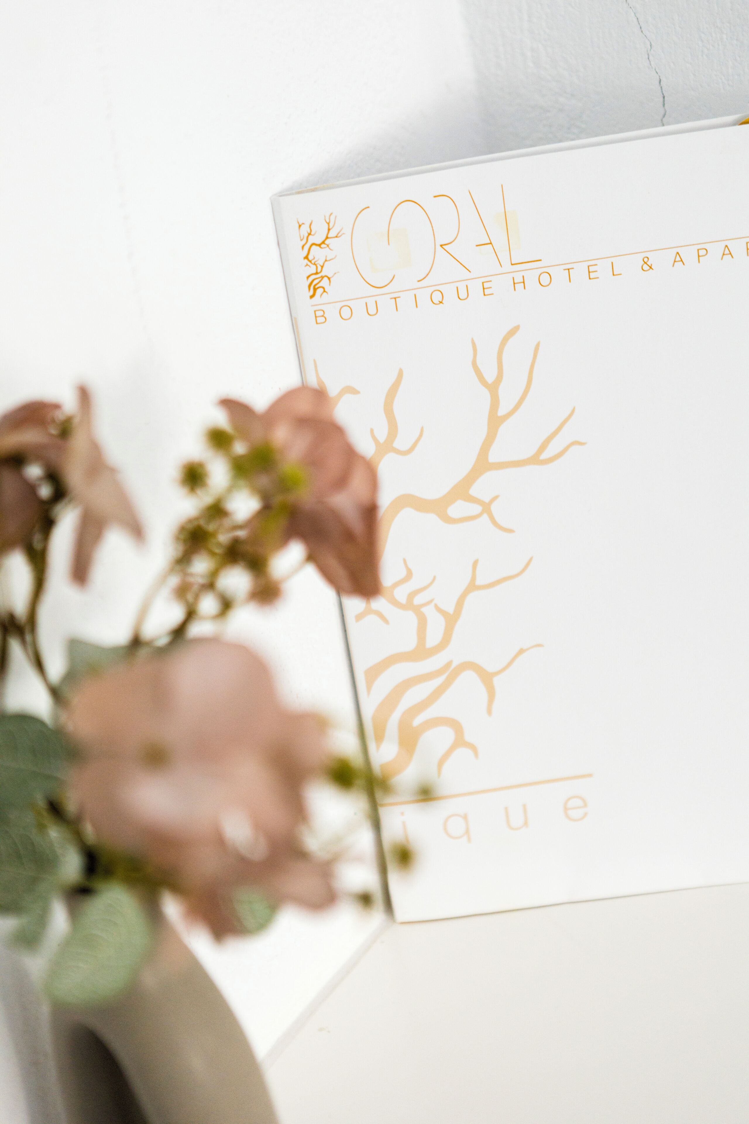 Un panneau blanc avec une inscription dorée indiquant « CORAL Boutique Hotel & Spa » et un motif décoratif représentant un arbre.