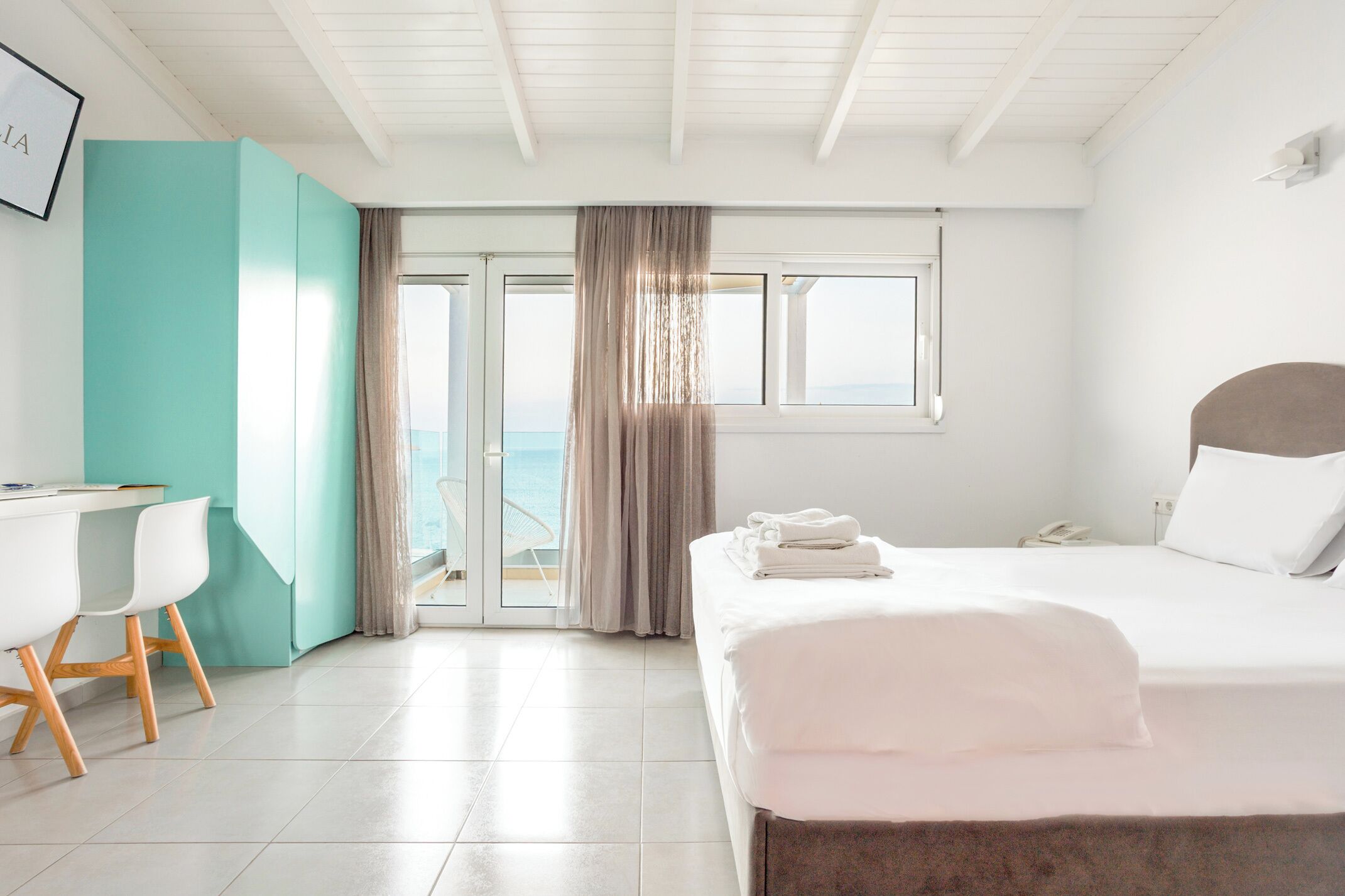 Habitación de hotel con cama, escritorio, silla, ventana con vistas y puerta que da a un balcón.