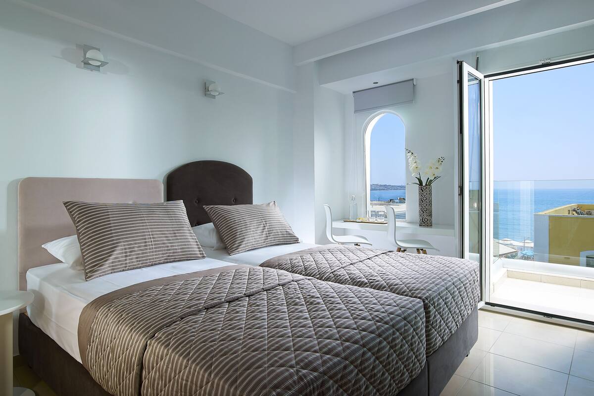 A bedroom with a bed, bedside table, and a view of the sea through a balcony door.