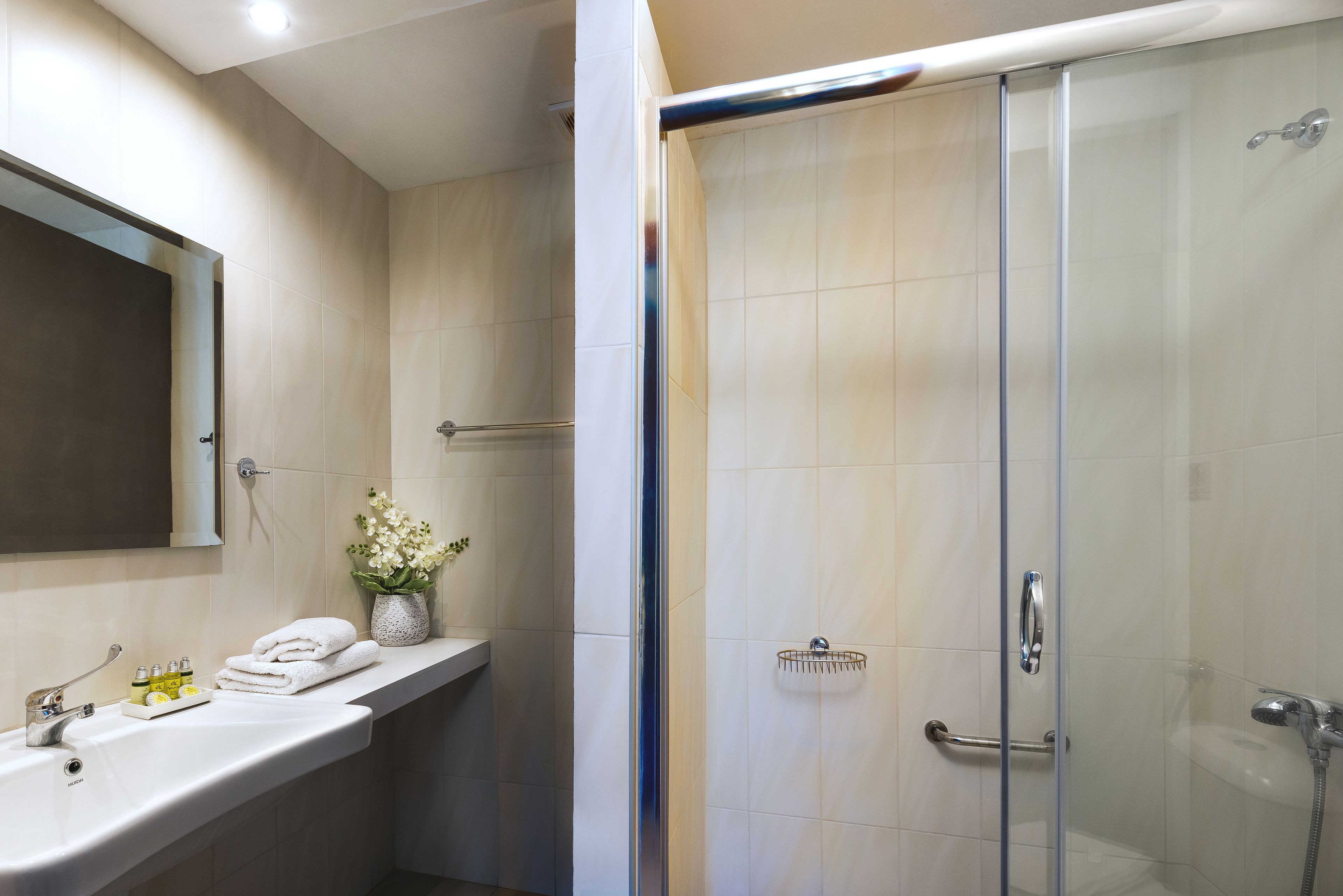 Un baño moderno con ducha de vidrio, tocador con espejo y estante con artículos de aseo.
