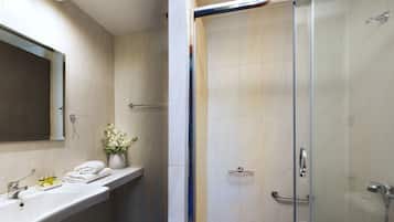 Un baño moderno con ducha de vidrio, tocador con espejo y estante con artículos de aseo.