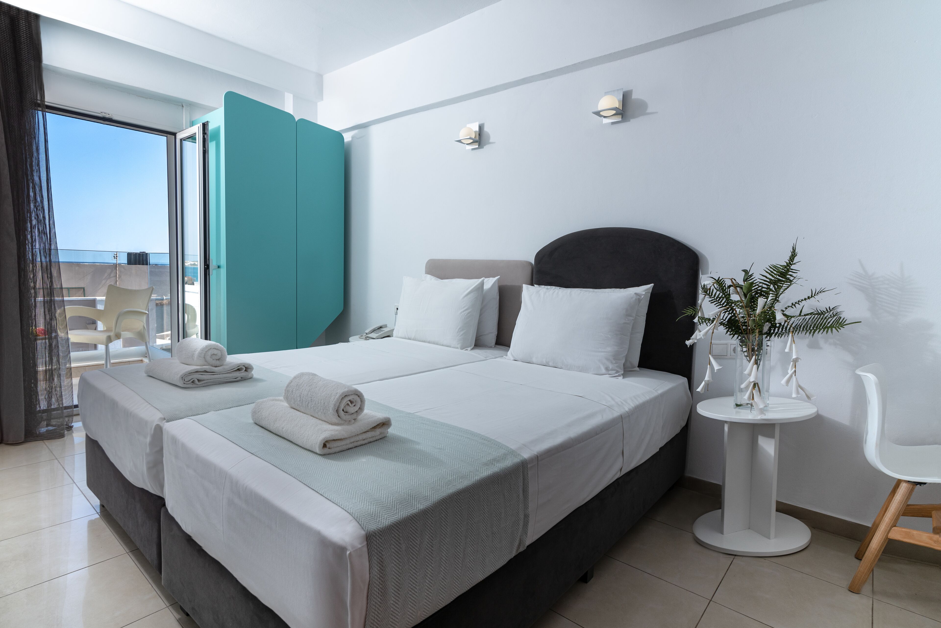 Una habitación de hotel moderna con dos camas, un balcón y una pequeña mesa redonda con una planta.