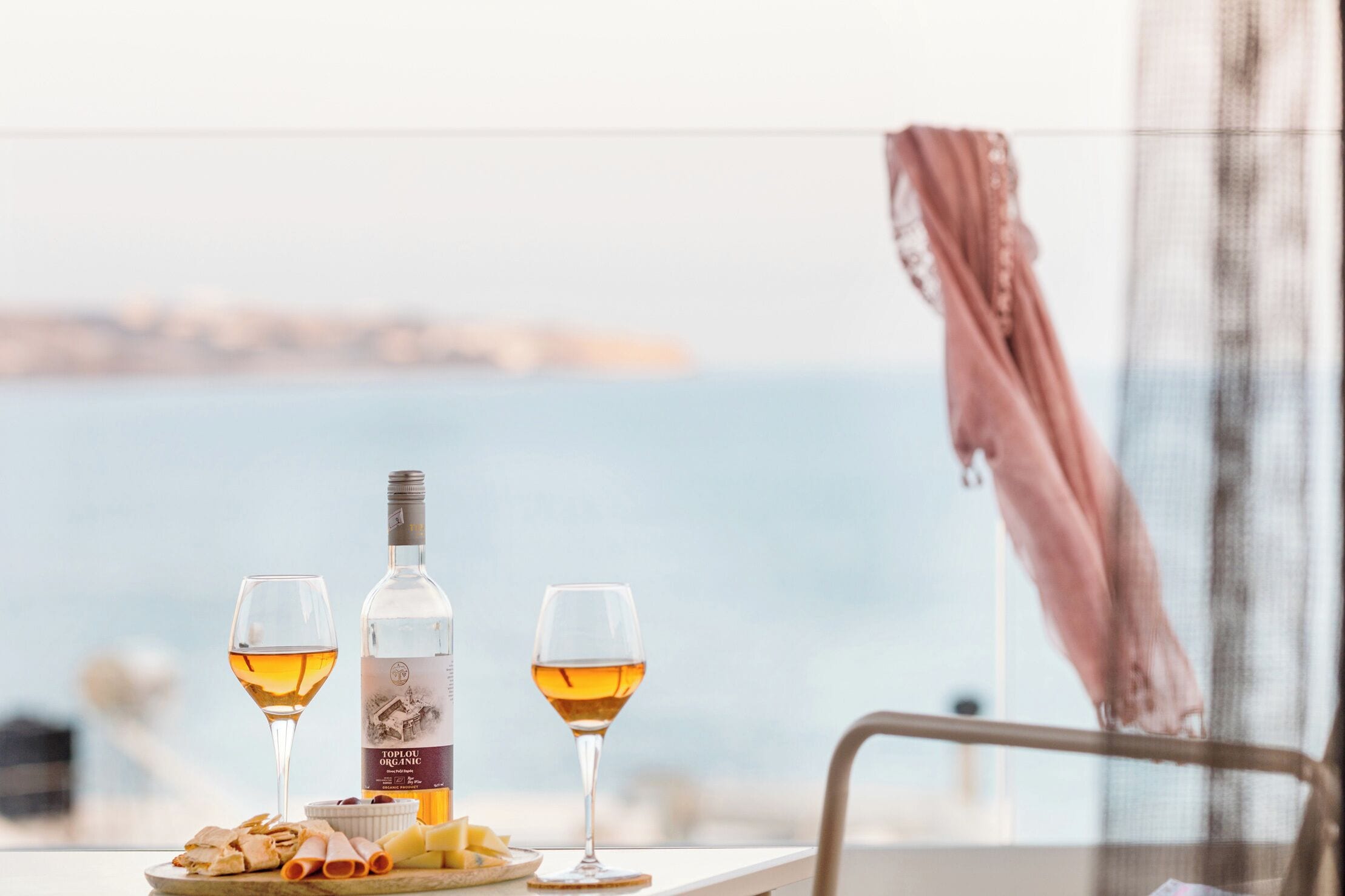 A table with a bottle of wine, two glasses, and a plate of cheese and crackers.