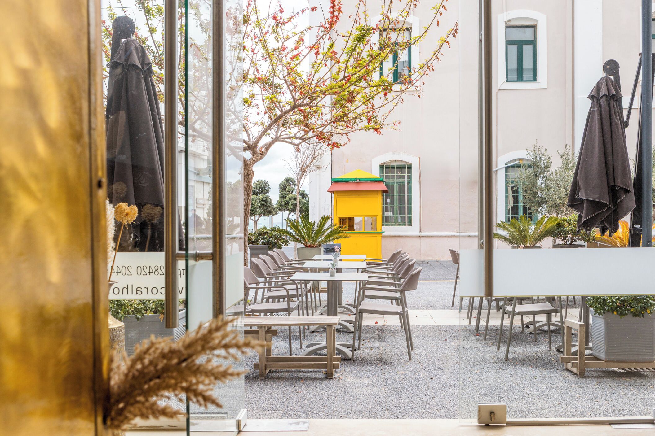 Un espace extérieur aménagé avec des tables et des chaises, un bâtiment jaune et une statue en arrière-plan.
