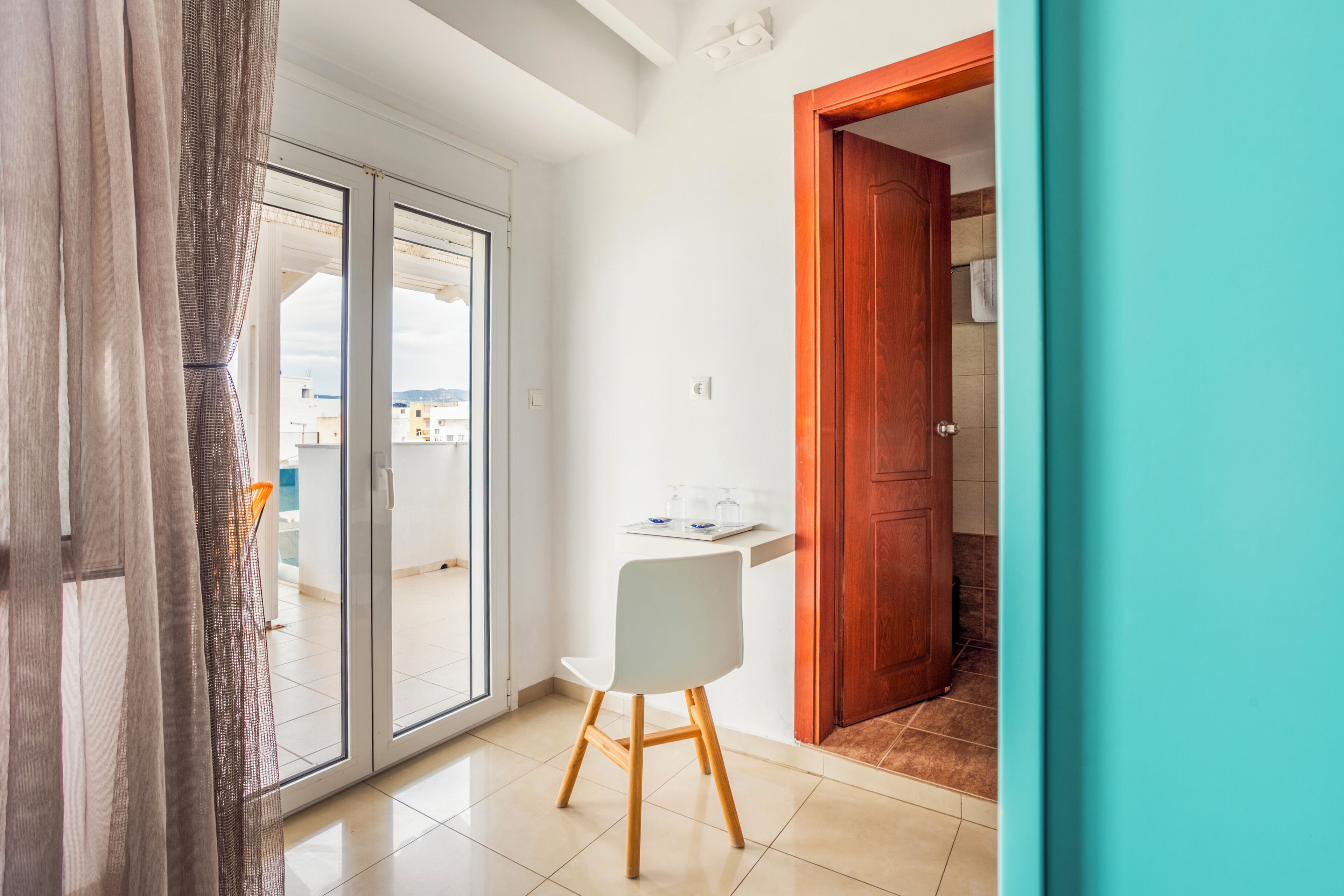 Una habitación con puerta corrediza de vidrio que da a un espacio exterior, una silla blanca y una puerta de madera.