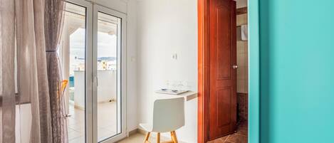 Una habitación con puerta corrediza de vidrio que da a un espacio exterior, una silla blanca y una puerta de madera.